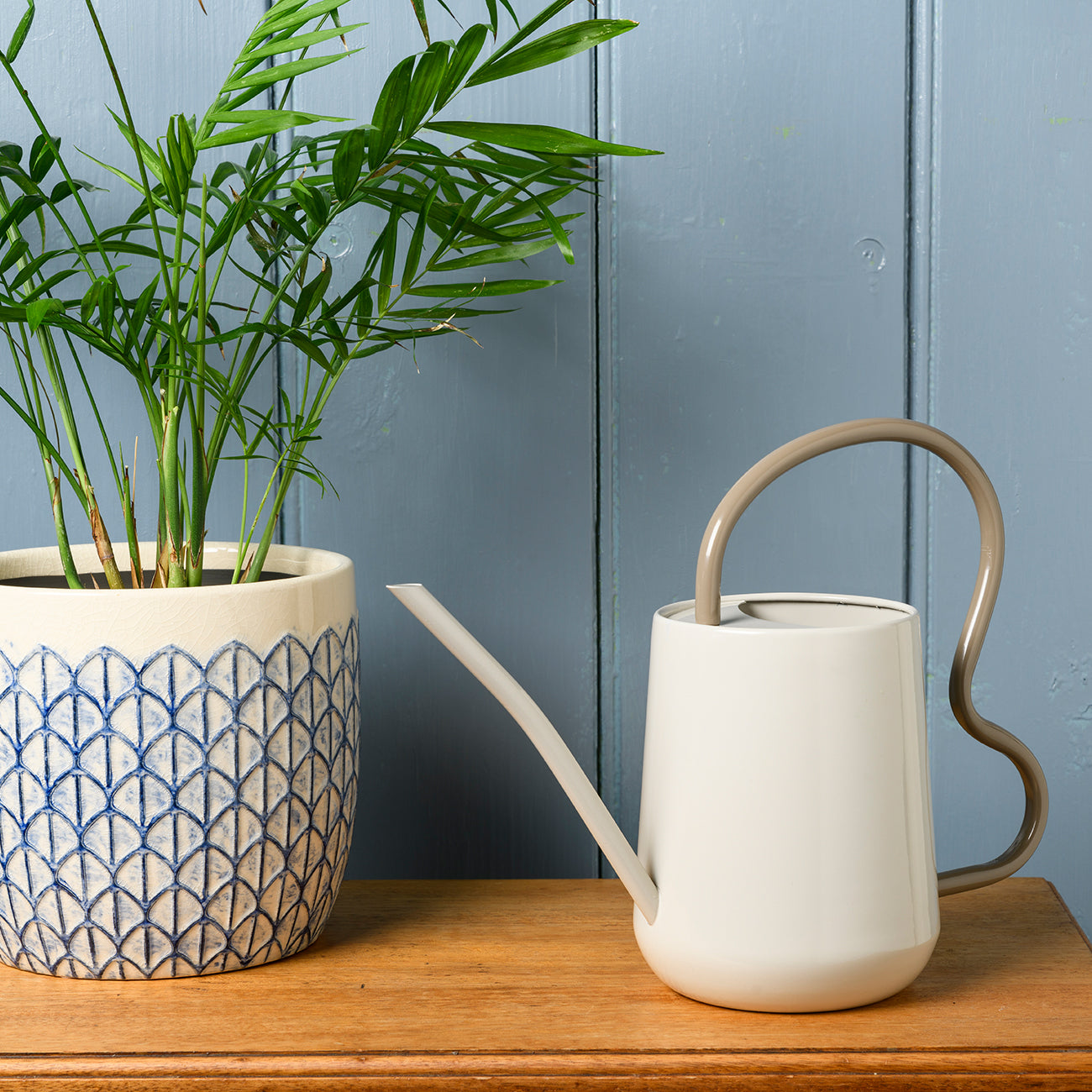 Stone Burgon & Ball indoor watering can next to a potted plant on a wooden surface.
