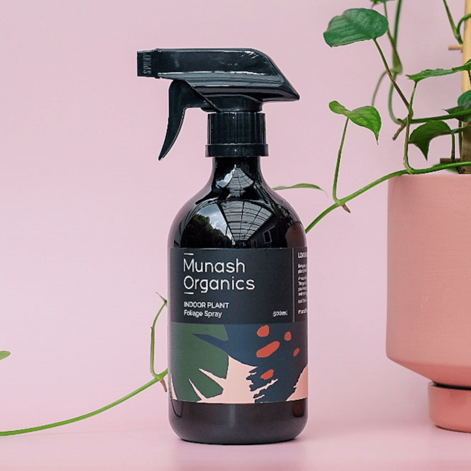 Munash Organics indoor plant care spray bottle with a pink background and plant elements.