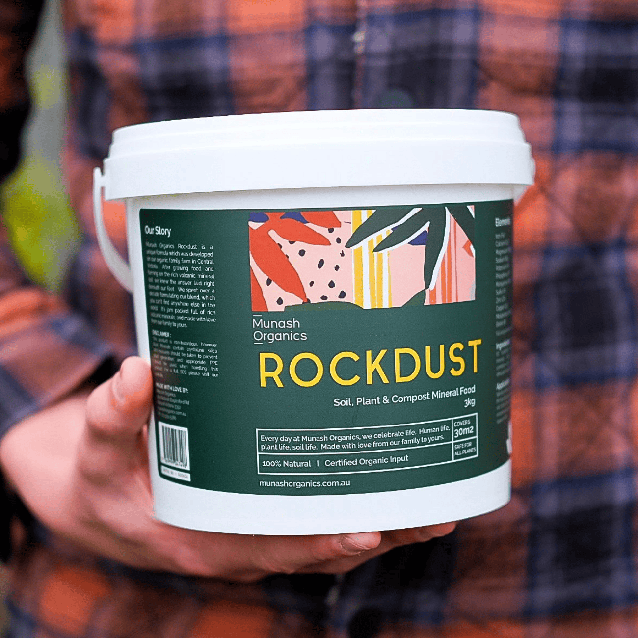 Person holding a container of Munash Organics Rockdust with a colourful label.