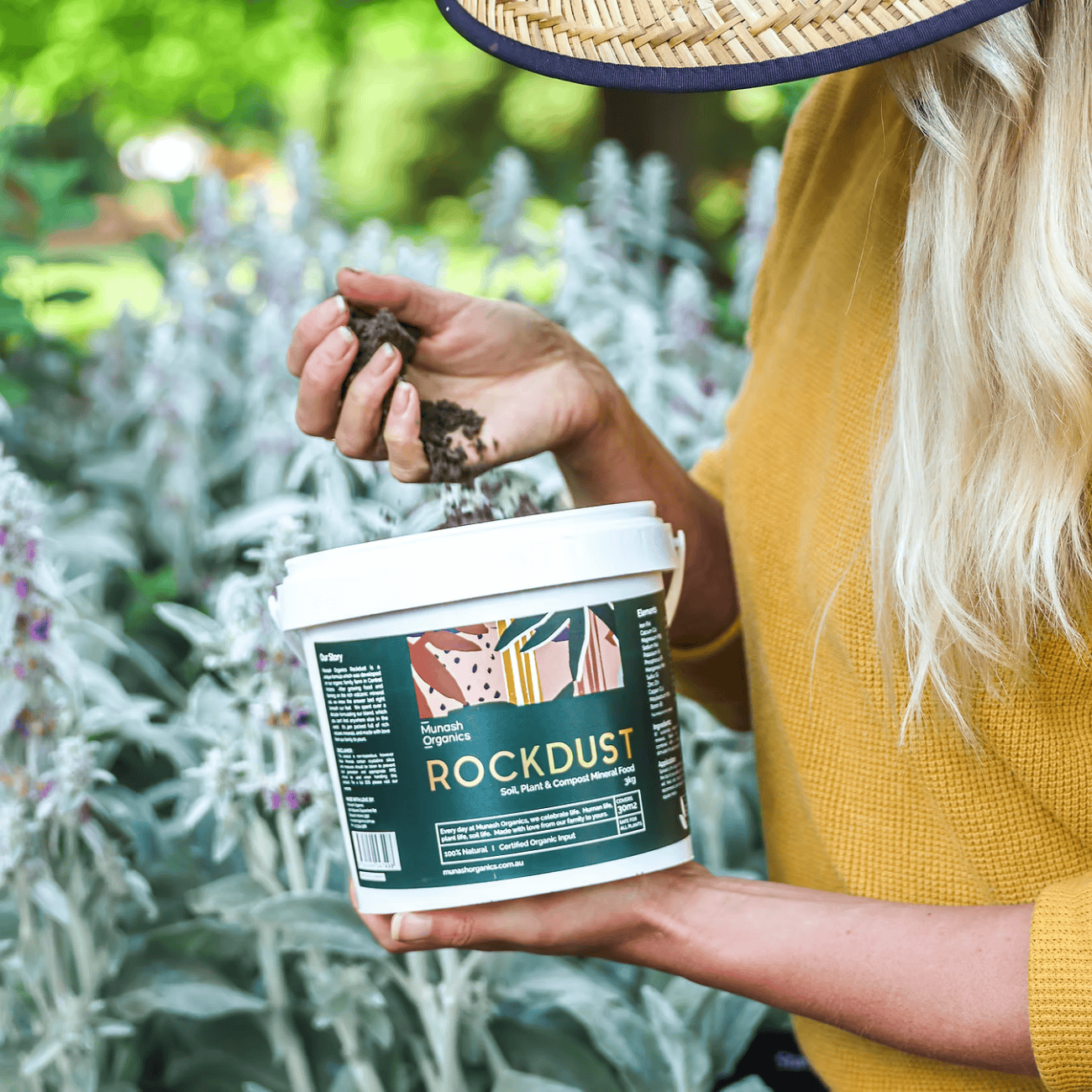Person holding a container of Munash Organics Rockdust in a garden setting.