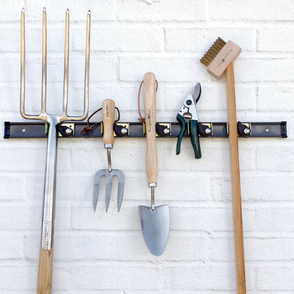 Set of gardening tools on a wall-mounted rack against a white brick wall.