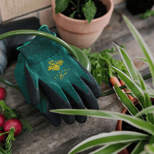 Keepers Enviro Bee Gardening Gloves surrounded by plants of potting bench.